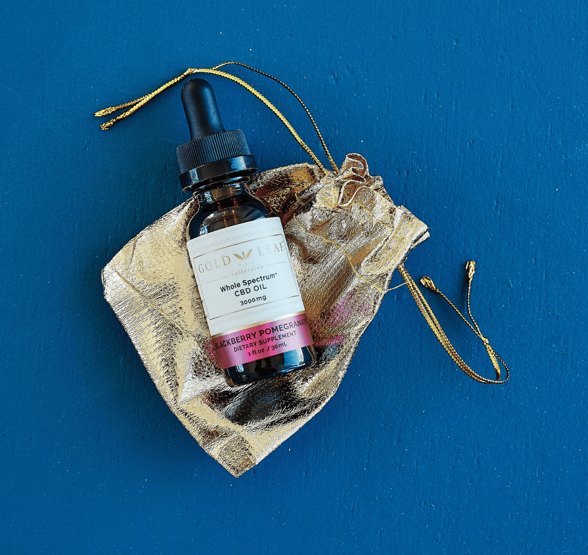 An opulent golden pouch with drawstrings, elegantly encasing a bottle of high-potency CBD tincture, set against a vivid blue backdrop, showing the product’s luxurious packaging