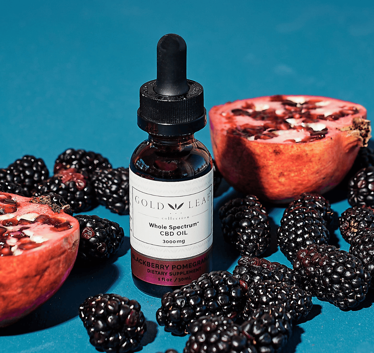 High-potency CBD tincture bottle presented with ripe pomegranates and blackberries against a soft blue background, evoking the product's blackberry pomegranate essence and featuring the label 'Whole Spectrum CBD Oil 3000mg.'
